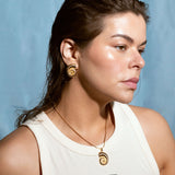 Woman wearing matching gold spiral earrings and necklace with swirl design, styled against a blue background.