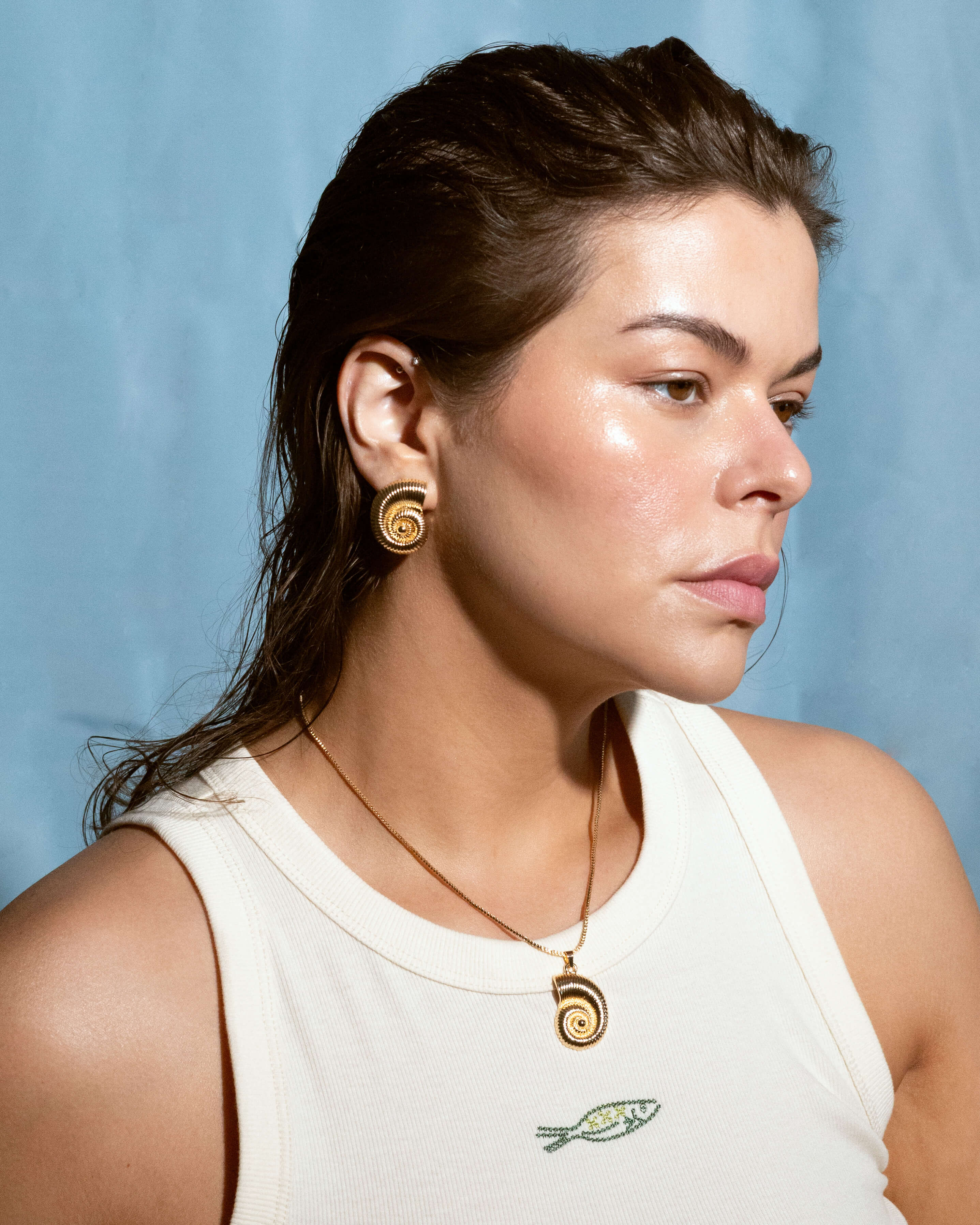 Woman wearing matching gold spiral earrings and necklace with swirl design, styled against a blue background.
