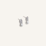 Pair of silver stud earrings with baguette crystal tops and pearl drops, displayed on a soft background.