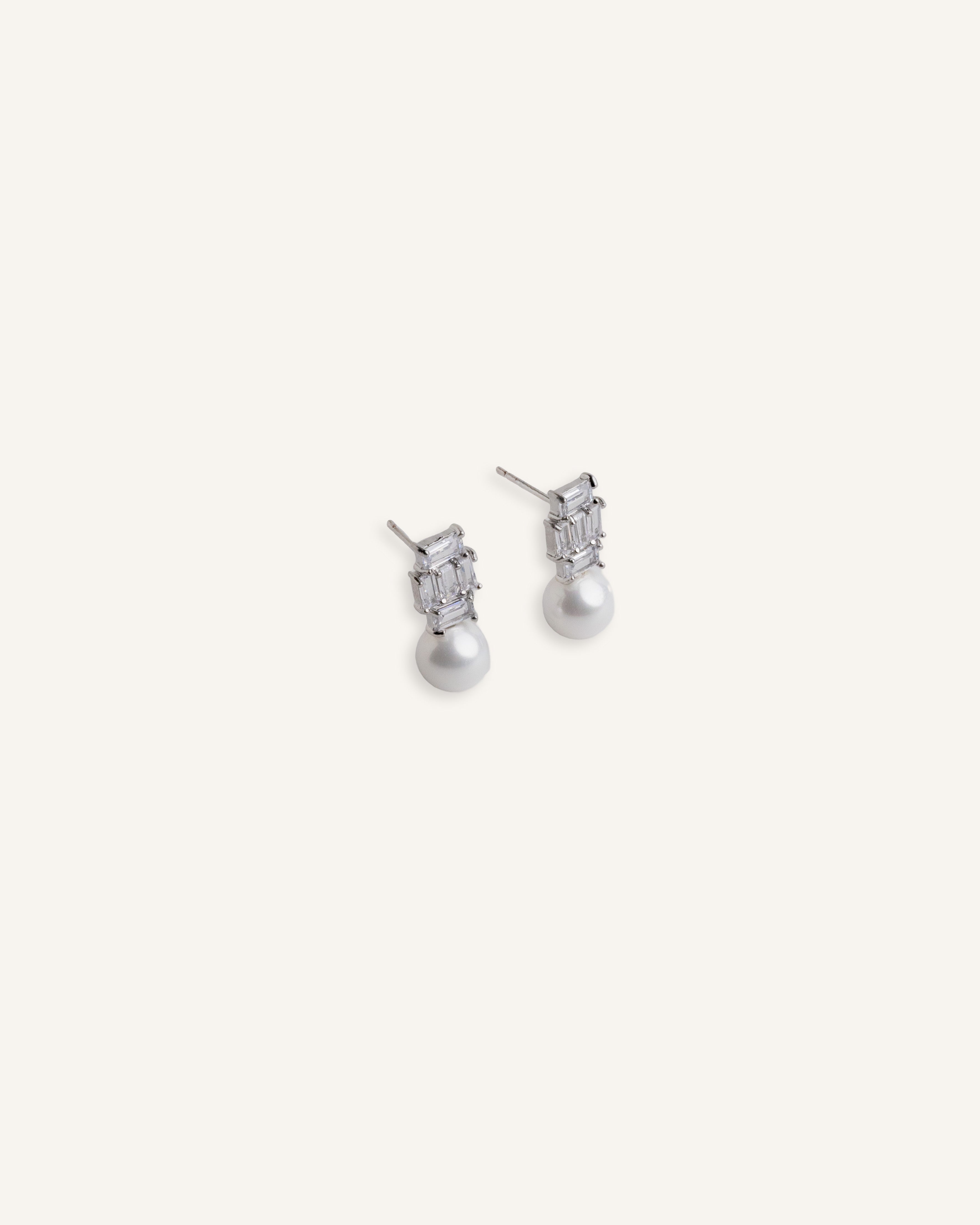 Pair of silver stud earrings with baguette crystal tops and pearl drops, displayed on a soft background.