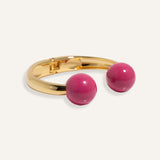 Gold open cuff bracelet with large enamel beads in pink and purple, styled for casual daywear..