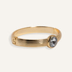  Gold cuff bracelet with ridged band and clear round gemstone at center.