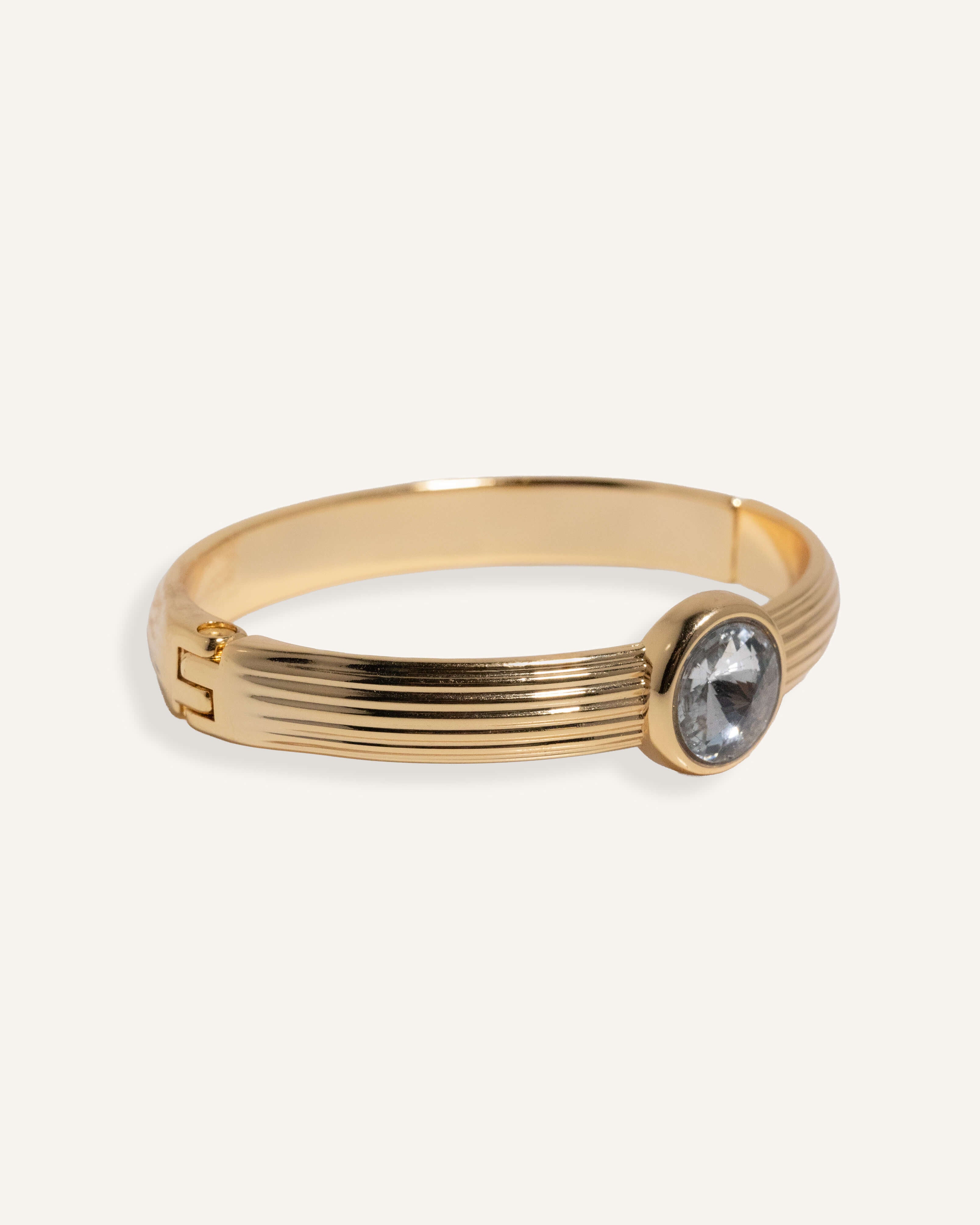  Gold cuff bracelet with ridged band and clear round gemstone at center.