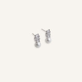 Pair of silver stud earrings with baguette crystal tops and pearl drops, displayed on a soft background.