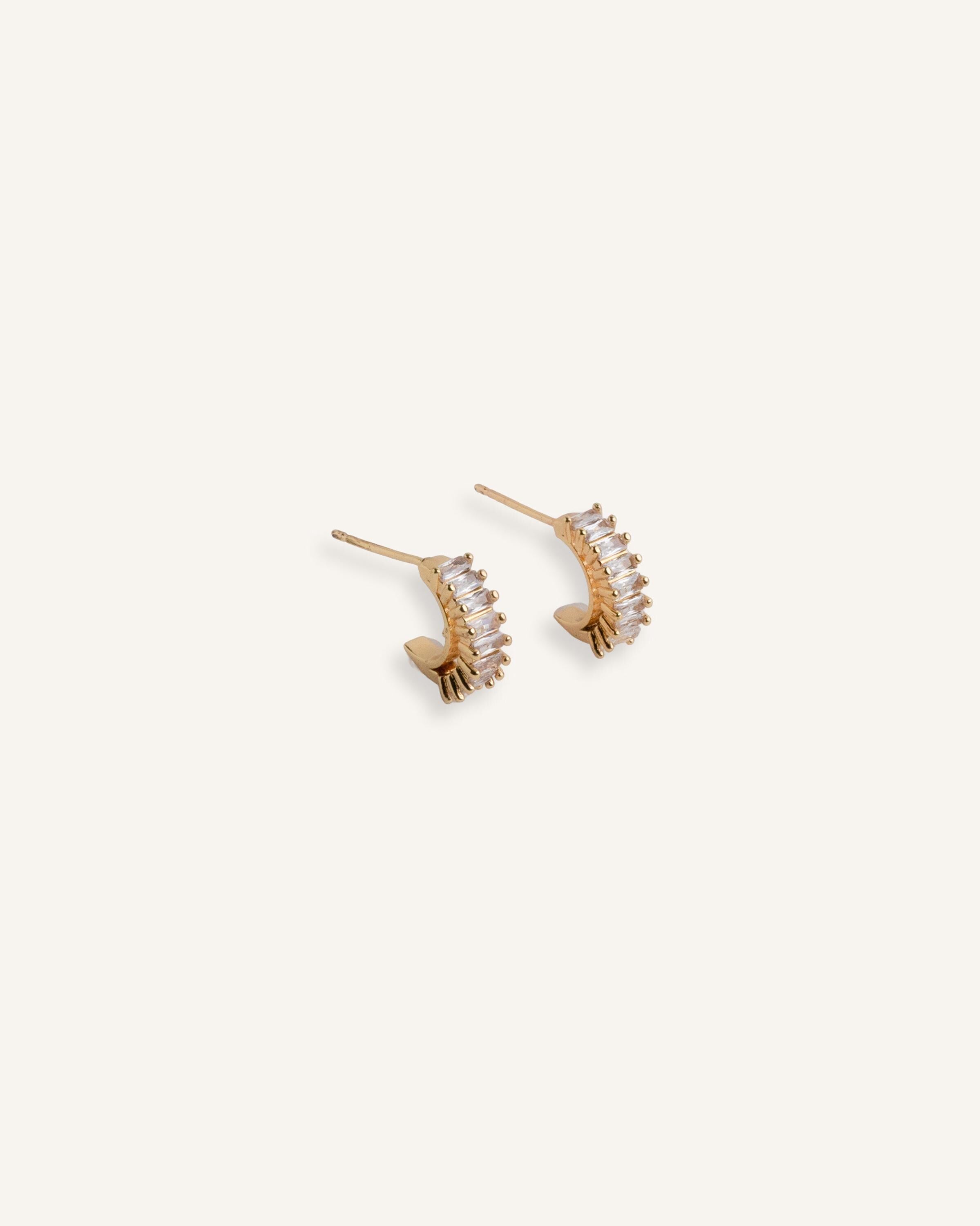 Pair of gold stud earrings with curved crystal fan design, displayed on a neutral background.