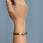 Gold plated bangle bracelet with grooved texture and a round clear crystal centerpiece – minimalist and elegant cuff for women