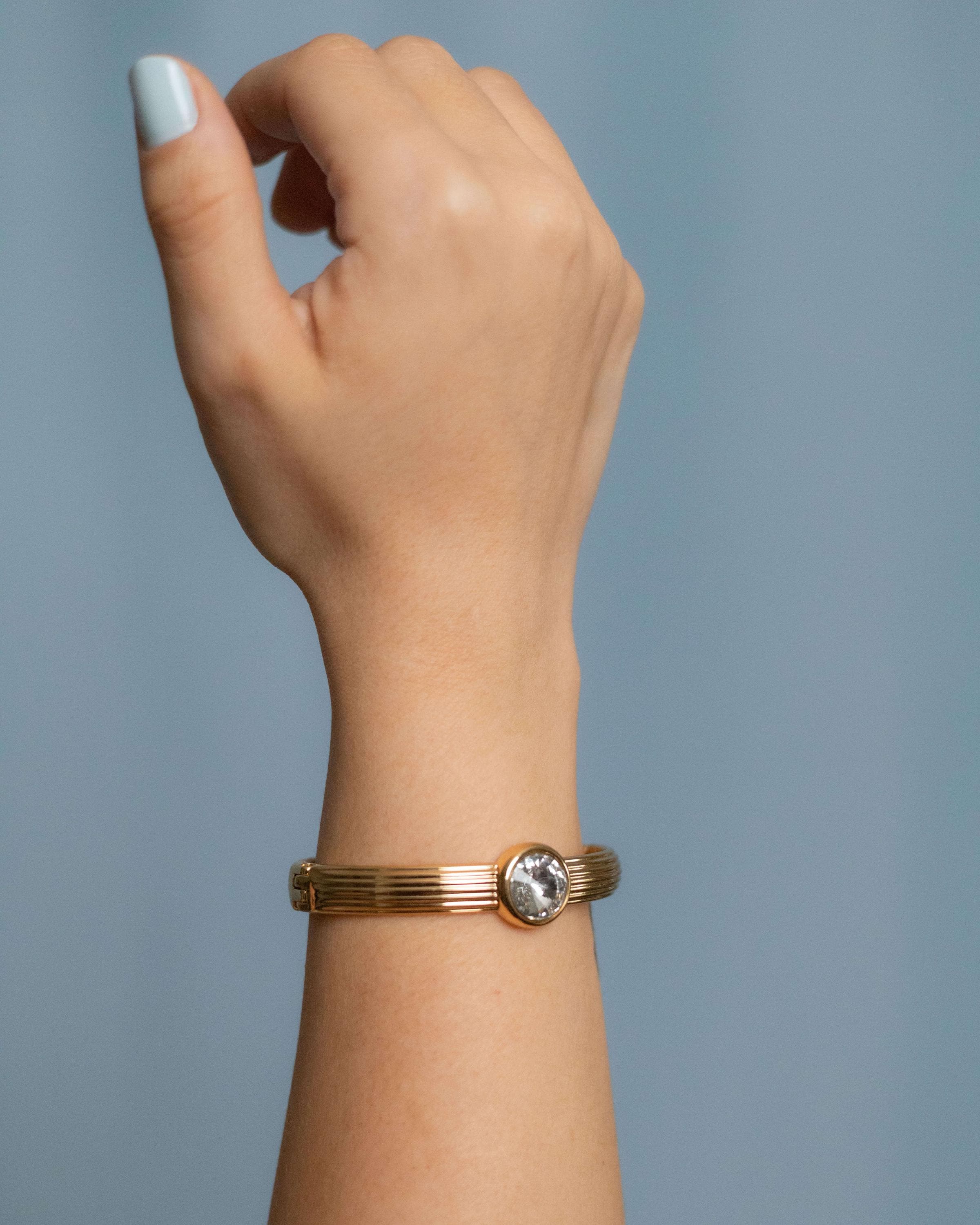 Gold plated bangle bracelet with grooved texture and a round clear crystal centerpiece – minimalist and elegant cuff for women