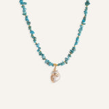 Turquoise beaded necklace with gold-accented shell pendant, shown flat against a neutral background.