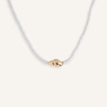 White beaded necklace with gold shell pendant, styled for summer jewelry collection.