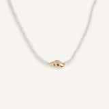 White beaded necklace with gold shell pendant, styled for summer jewelry collection.