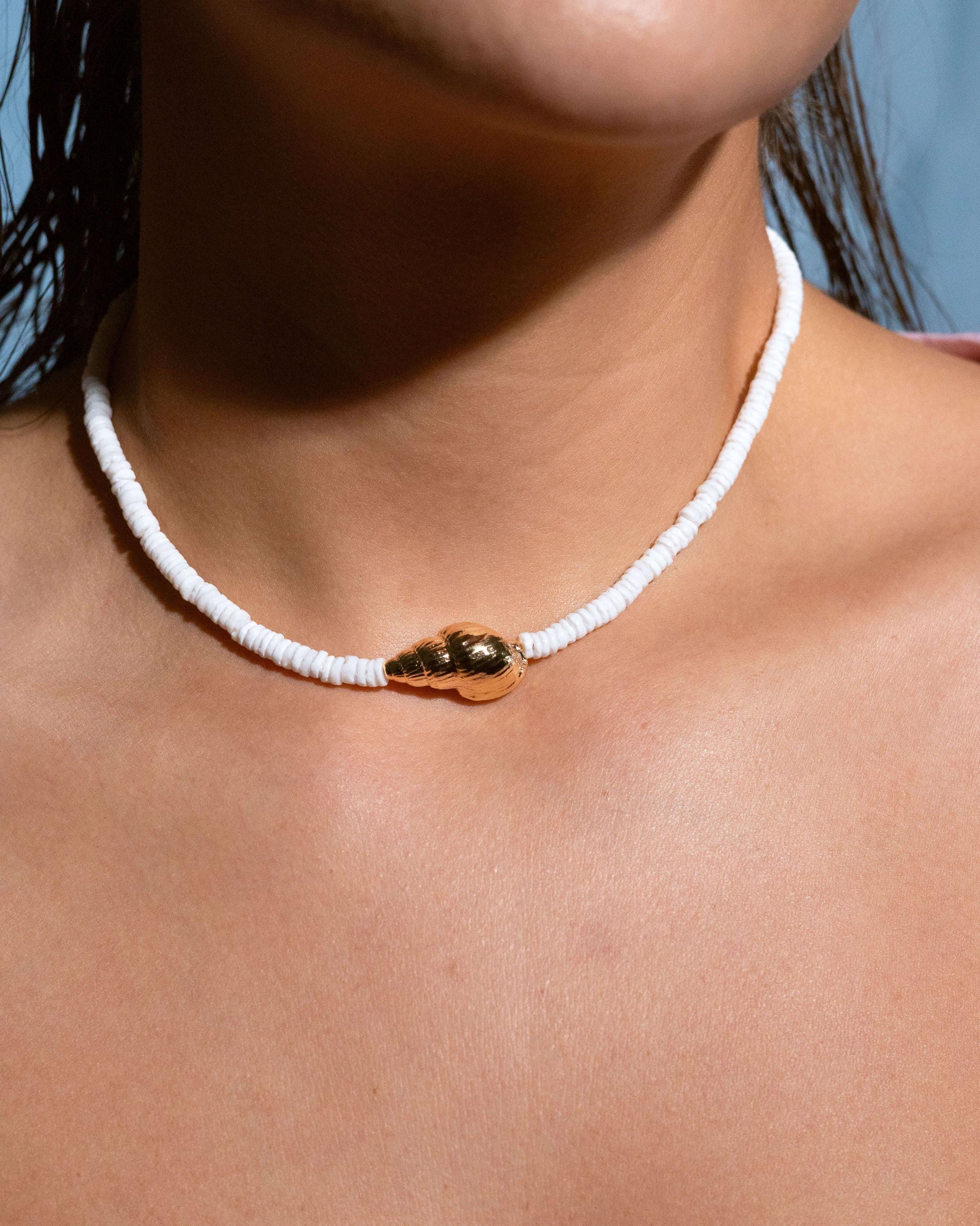 Model wearing dainty white beaded necklace with gold shell charm, casual summer jewelry for beach days, vacation outfit accessory