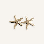 Close-up of gold starfish earrings on a white background, showing matte texture and summer-inspired design.
