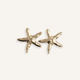 Close-up of gold starfish earrings on a white background, showing matte texture and summer-inspired design.