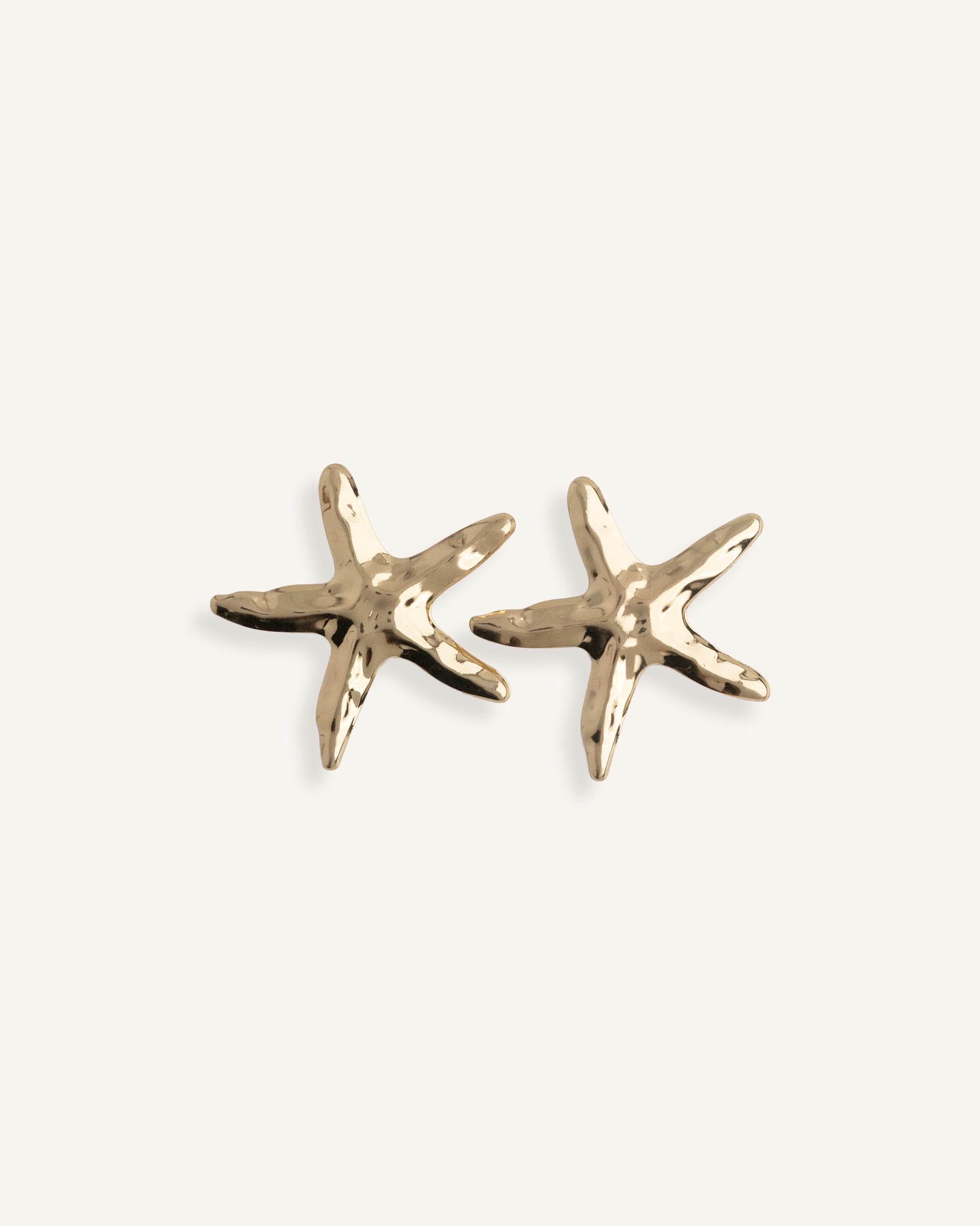 Close-up of gold starfish earrings on a white background, showing matte texture and summer-inspired design.
