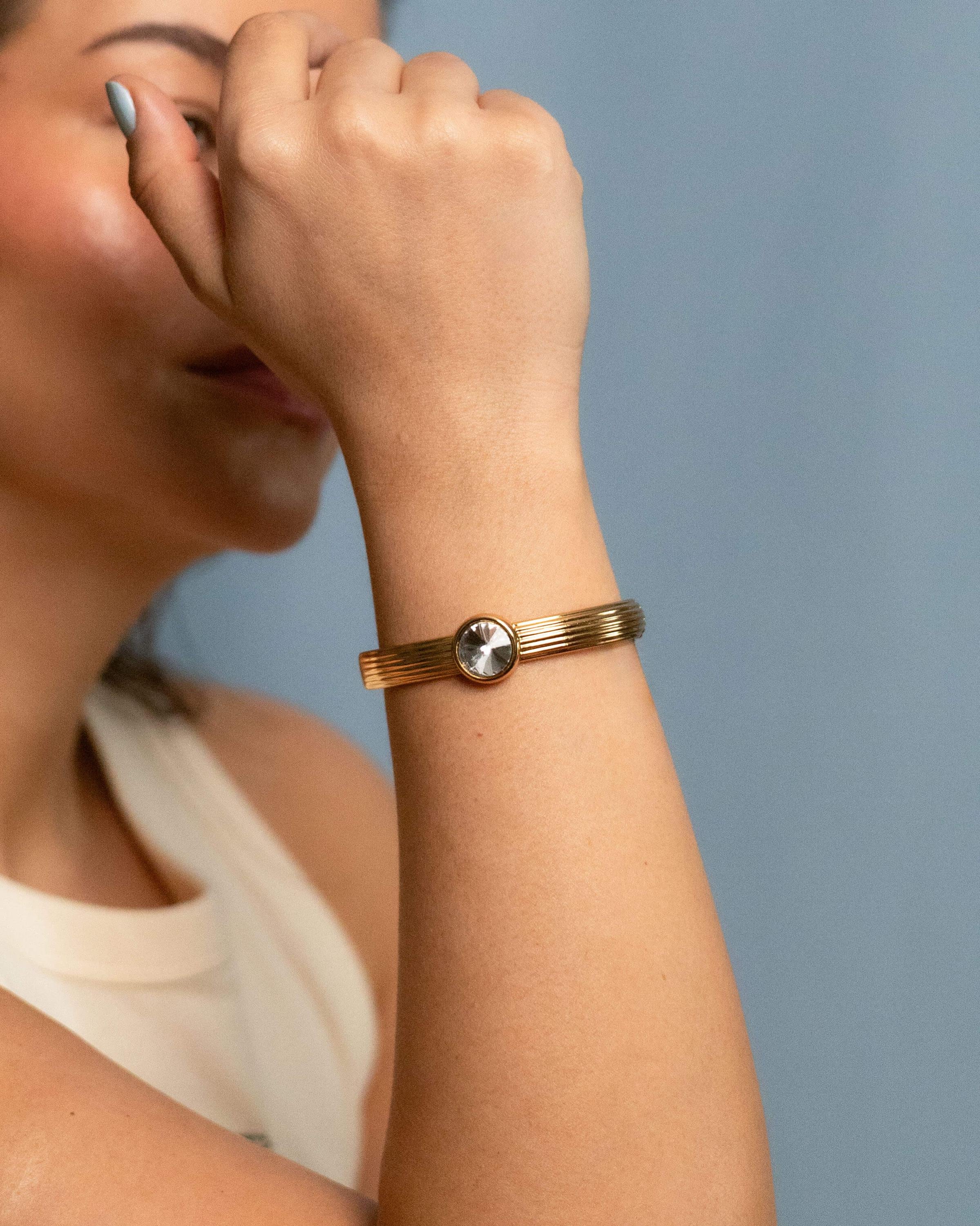 Gold plated bangle bracelet with grooved texture and a round clear crystal centerpiece – minimalist and elegant cuff for women.