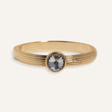 Gold cuff bracelet with ridged band and clear round gemstone at center
