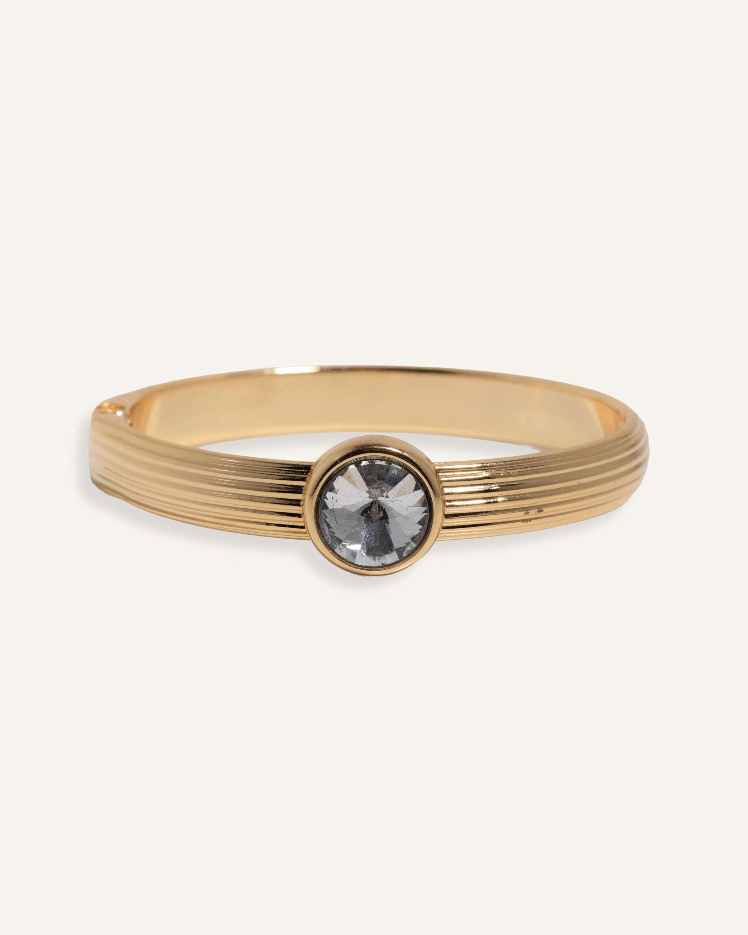 Gold cuff bracelet with ridged band and clear round gemstone at center